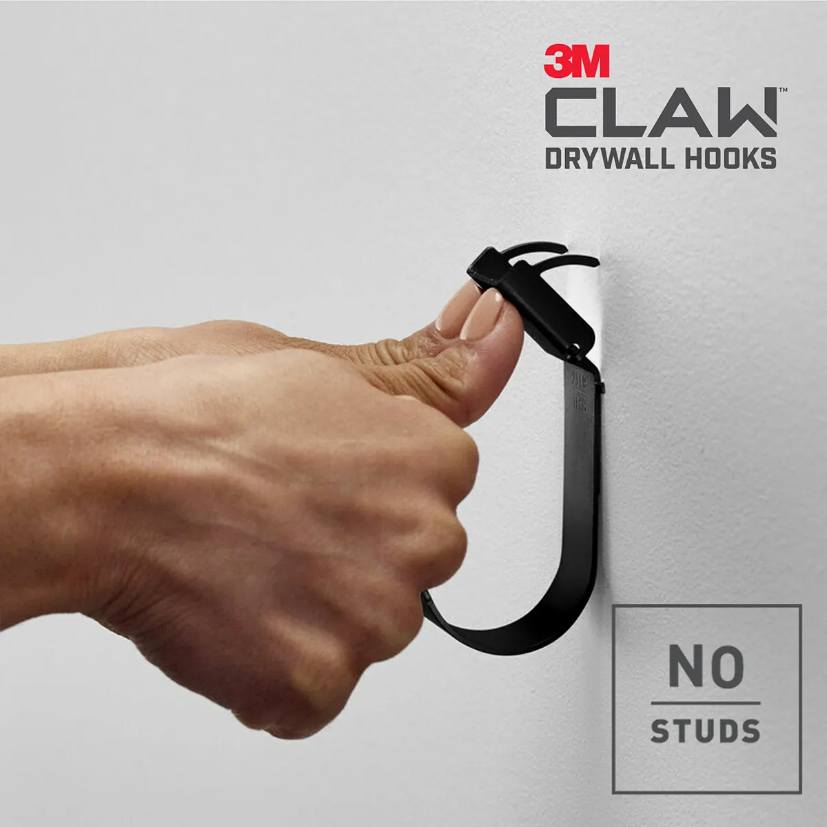 Þumlar þrýsta stálfestingu 3M CLAW snaga inn í gifsvegg.
